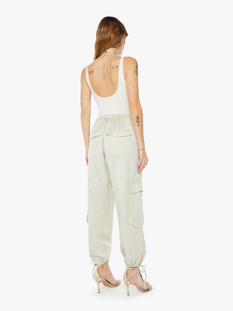 Back view of a woman wearing a light green cargo pant with an elastic tie waist and hem, large side pockets, paired with a white tank top.