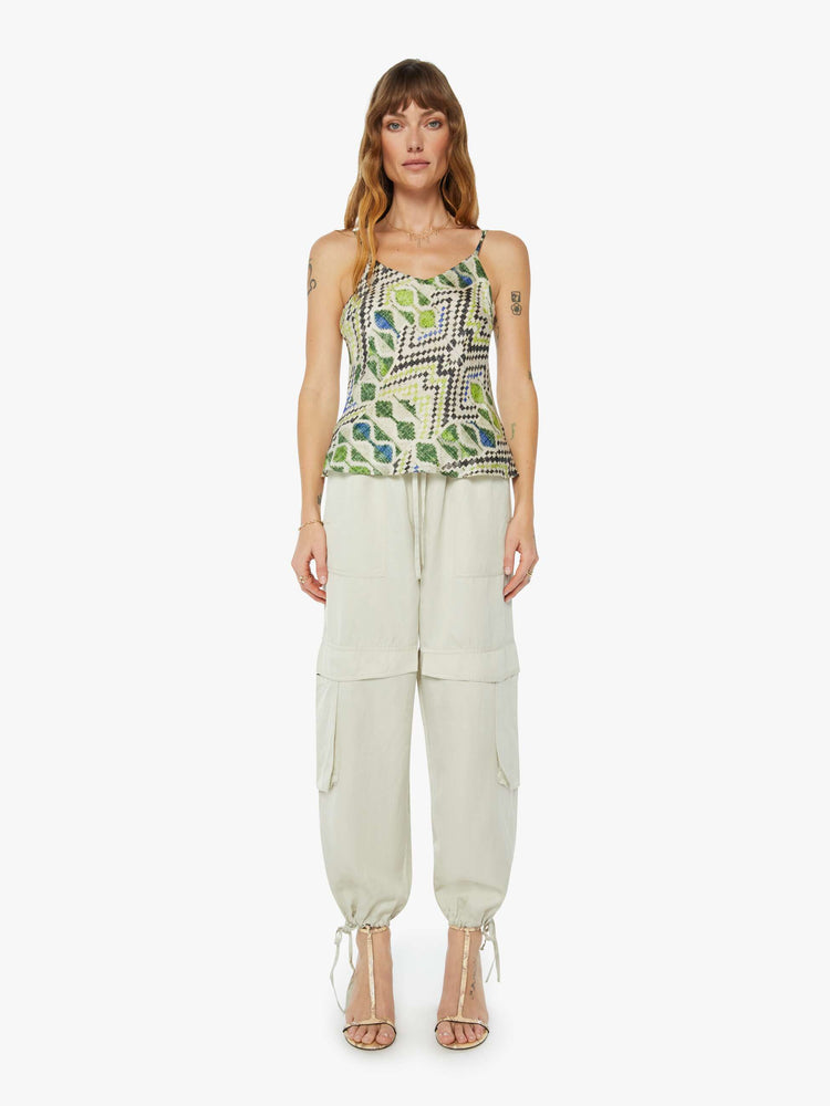 A front full body view of a woman wearing a spaghetti strap top featuring a green multi color pattern, paired with a pale green cargo pant.