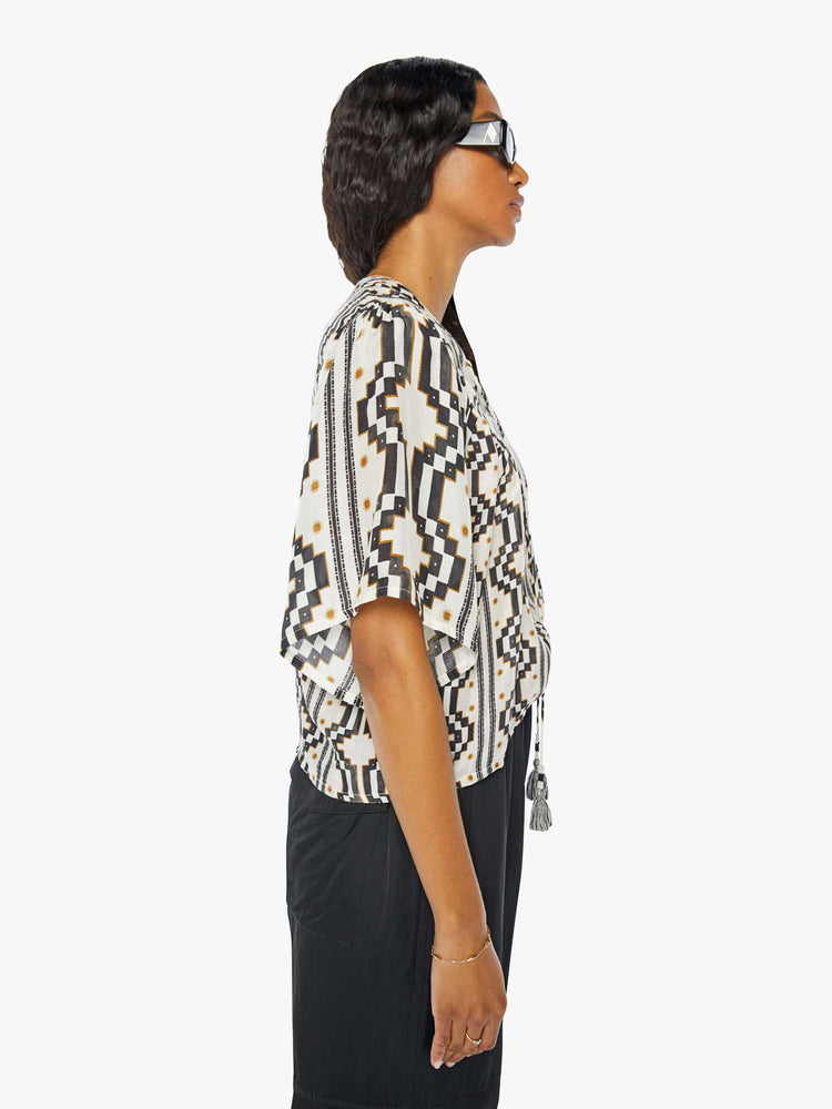 A side view of a woman wearing a black and white pattern short sleeve blouse featuring a flowy fit, paired with a black cargo pant.