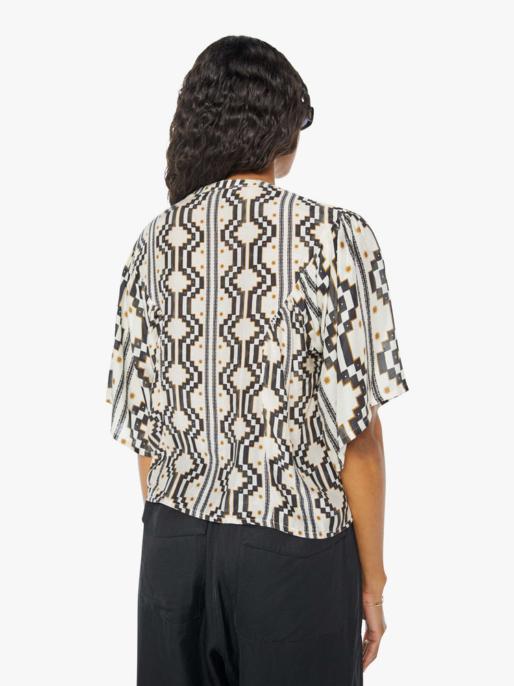 A back view of a woman wearing a black and white pattern short sleeve blouse featuring a flowy fit, paired with a black cargo pant.