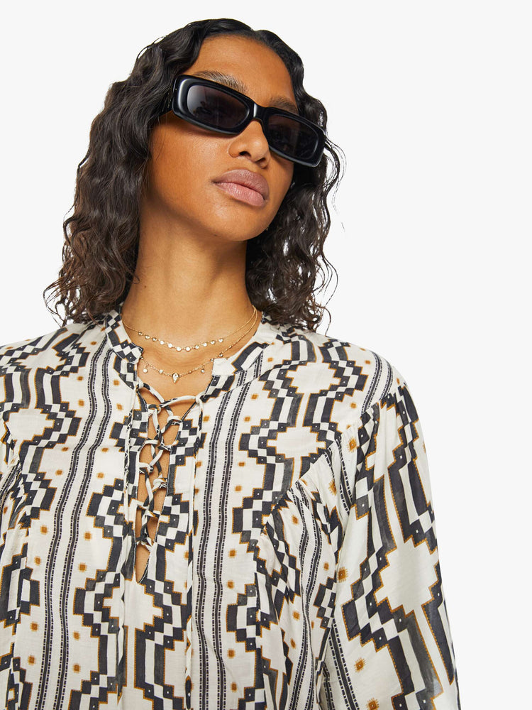 A front close up view of a woman wearing a black and white pattern short sleeve blouse featuring a laced v-neck with tassels and a flowy fit.