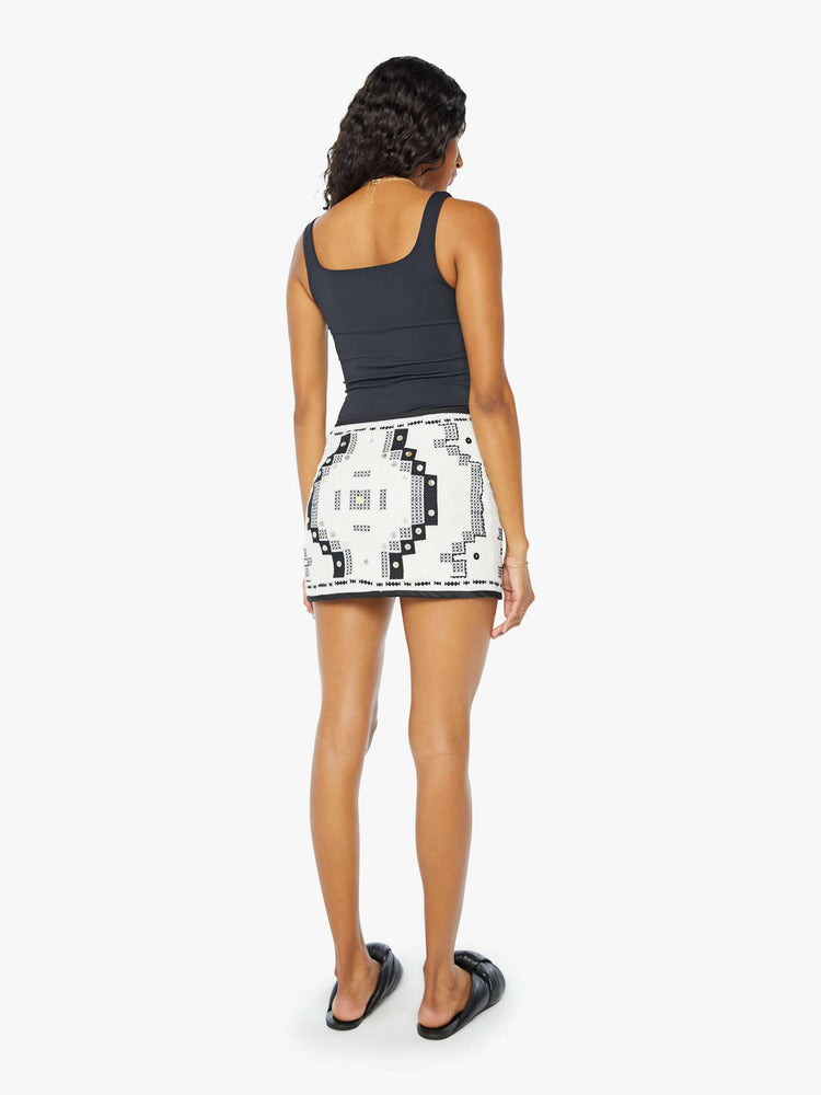 A back view of a woman wearing a short mini skirt with a black and white geometric pattern and contrast black trim, paired with a black tank top.