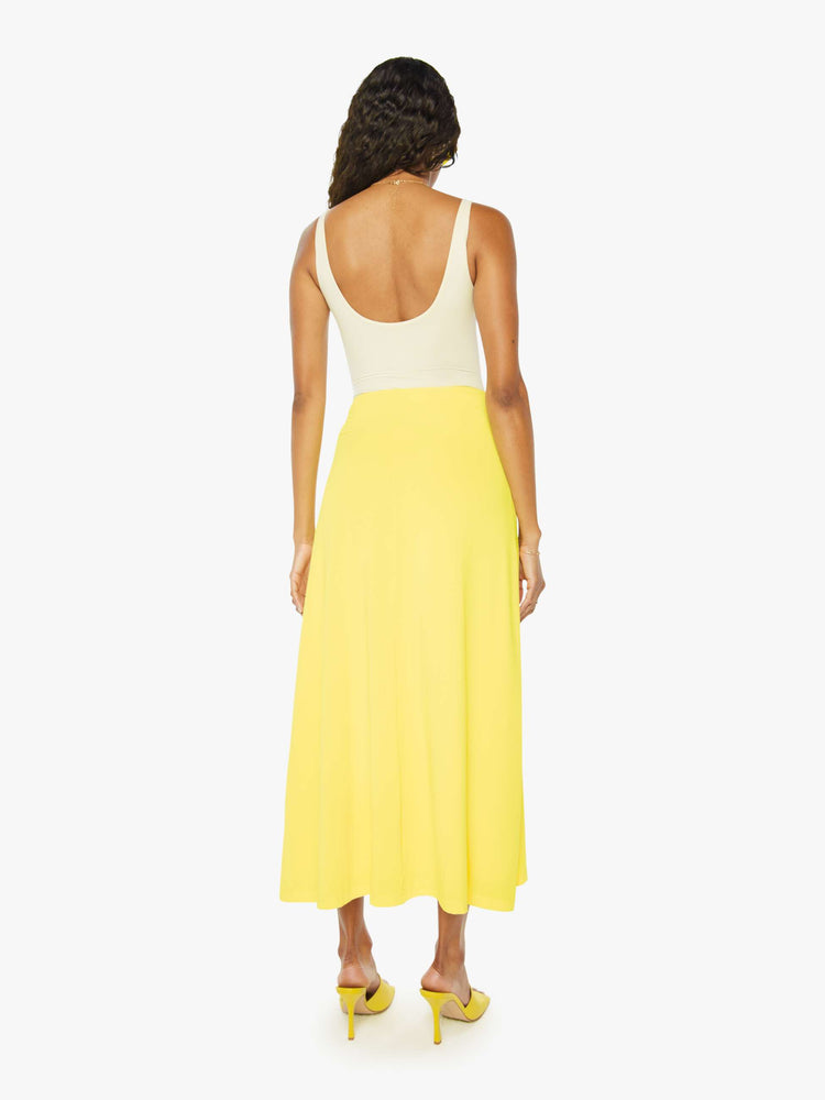 A back view of a woman wearing a bright yellow skirt with a flowy fit, paired with a white tank top.