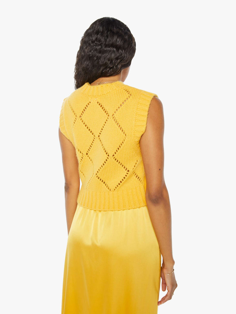 Back view of woman wearing a yellow skirt with a yellow knit sweater vest, featuring a diamond pattern.