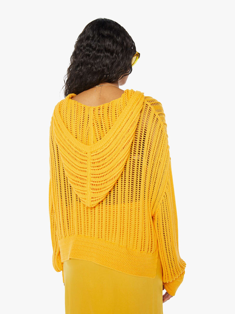 Back view of a woman wearing a loose knit, yellow sweater featuring a hood and an oversized fit.