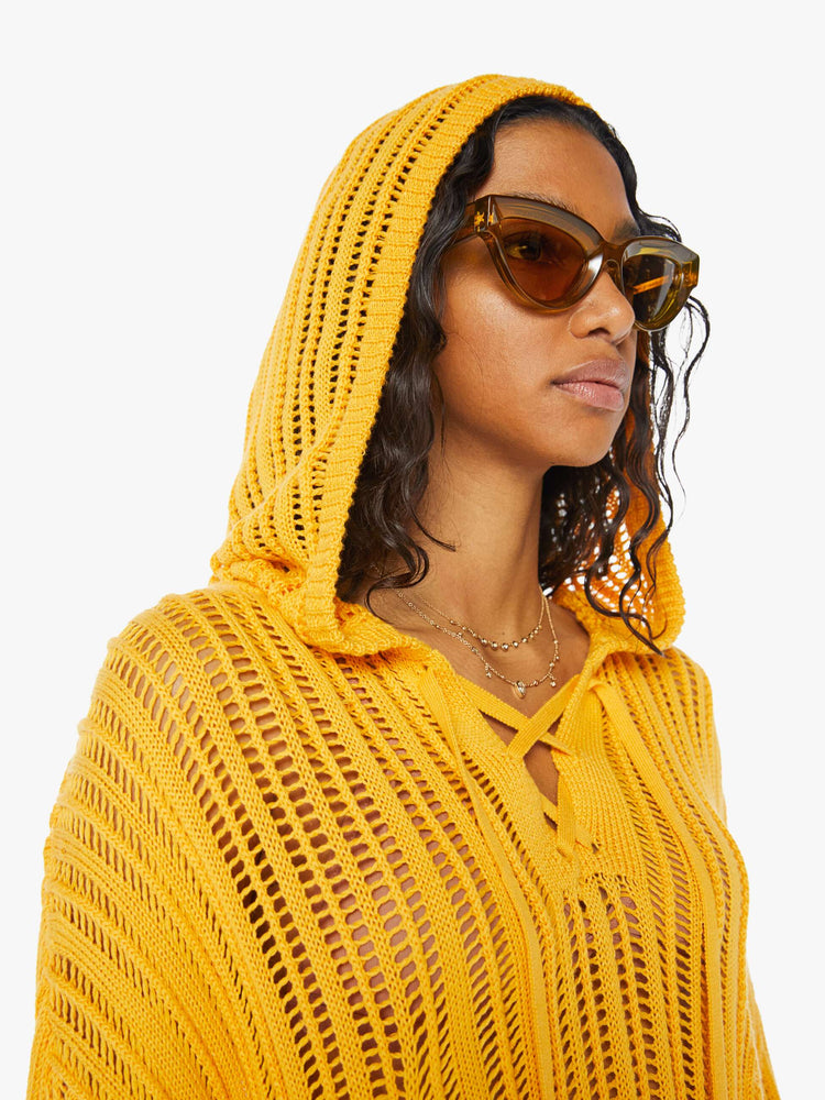 Front close up view of a woman wearing a loose knit, yellow sweater featuring a hood, a lace up v neck, and an oversized fit.