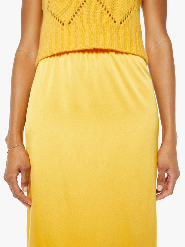 Front close up view of a woman wearing a yellow mid length skirt with a yellow knit vest.