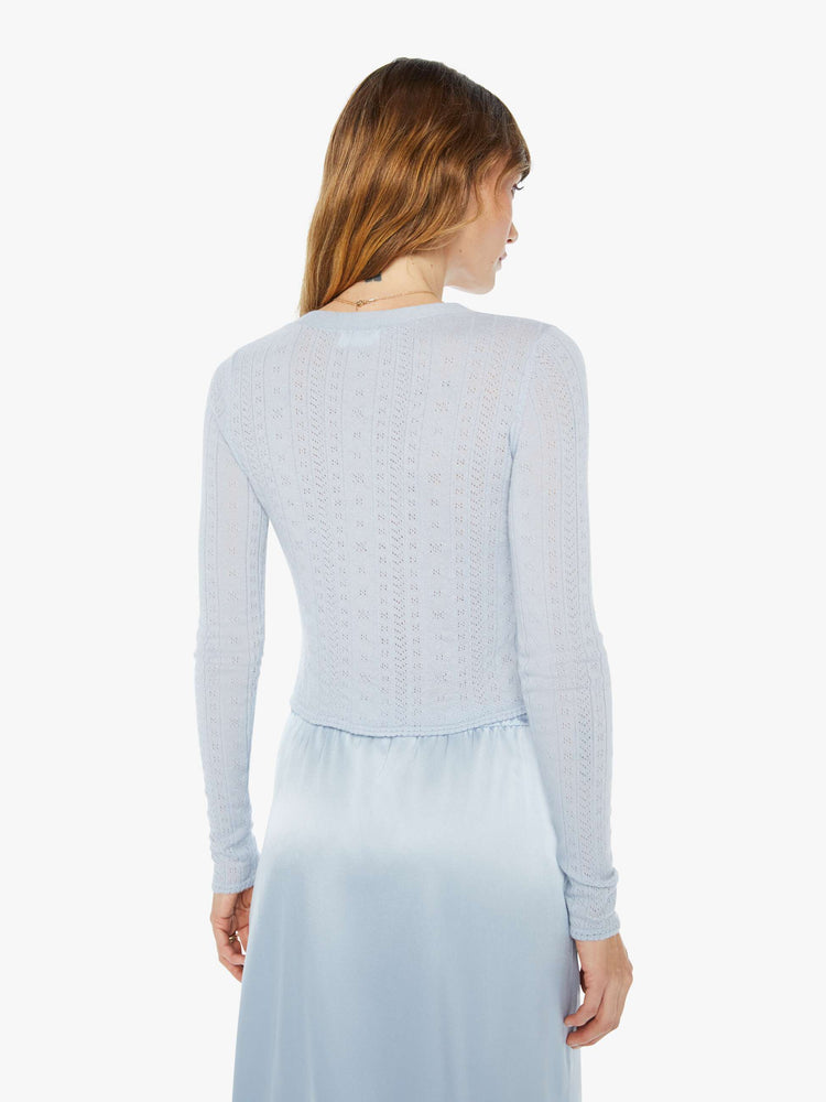 A back view of a woman wearing a light blue skirt with a light blue knit cardigan with a fitted and cropped fit.