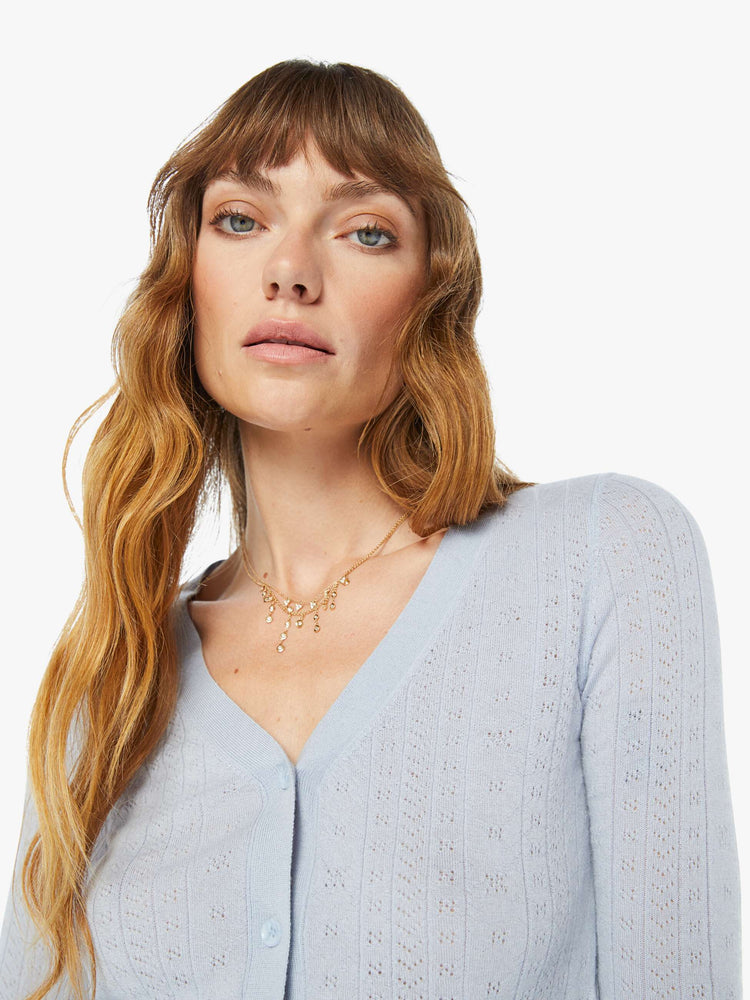 A front close up view of a woman wearing a light blue knit cardigan with a fitted and cropped fit.