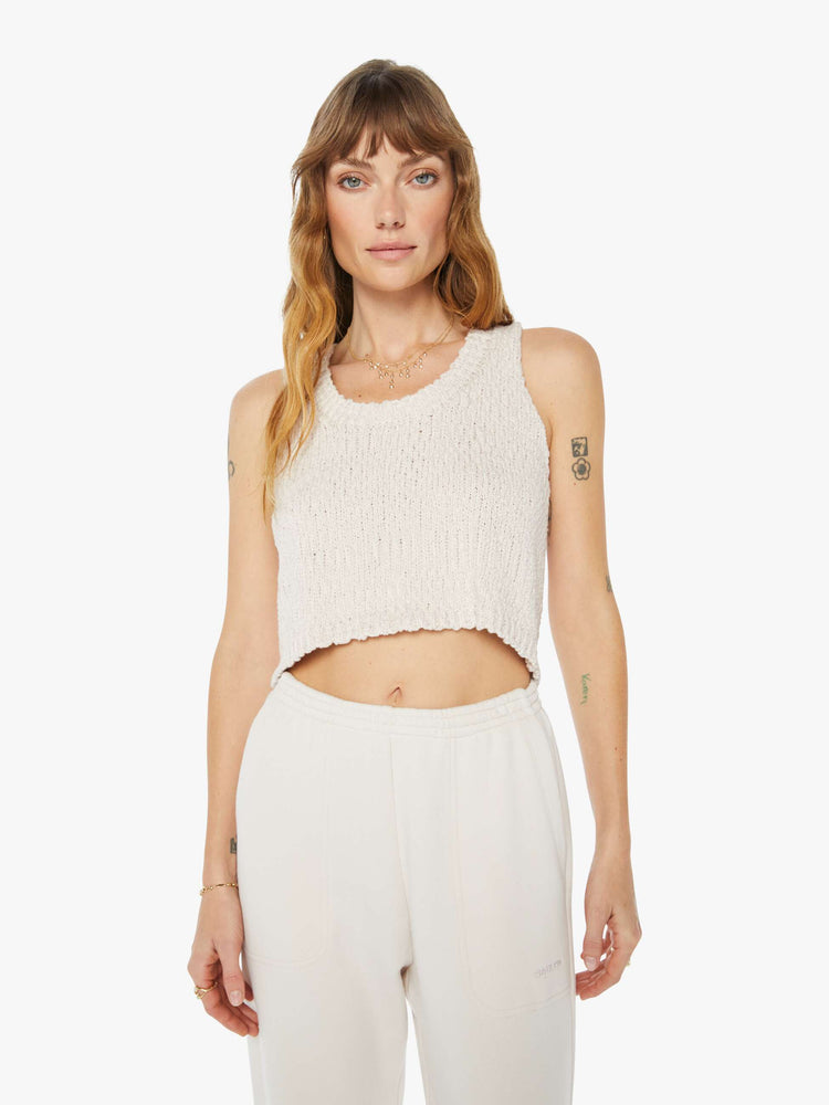 Front view of a woman wearing a knit tank in an off white hue, featuring a cropped body.