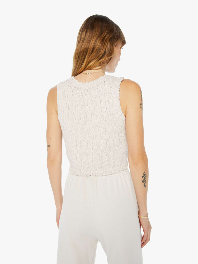 Back view of a woman wearing a knit tank in an off white hue, featuring a cropped body.