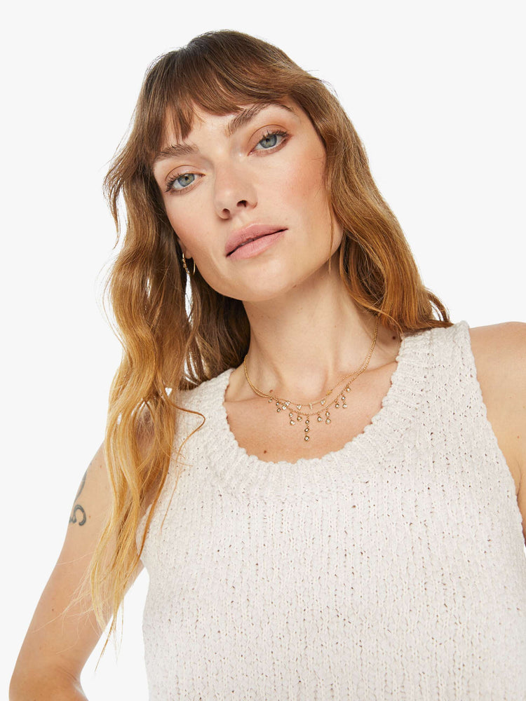 Front close up view of a woman wearing a knit tank in an off white hue, featuring a cropped body.