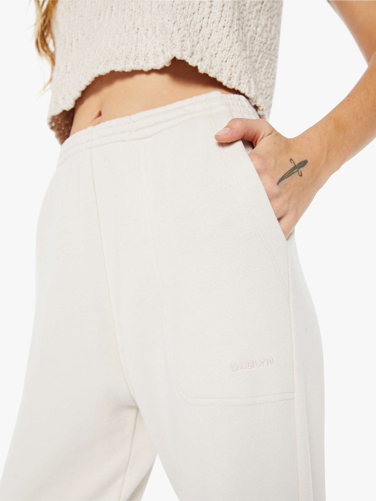 Front close up view of a woman wearing an off white pair of sweatpants featuring a high rise, paired with a knit off white tank.