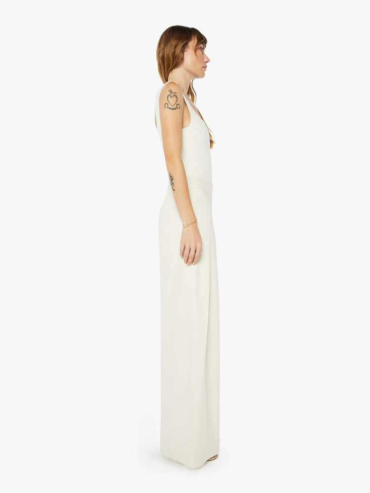 Side view of a womens off white pant featuring a high rise, a pleated wide leg, and long inseam.