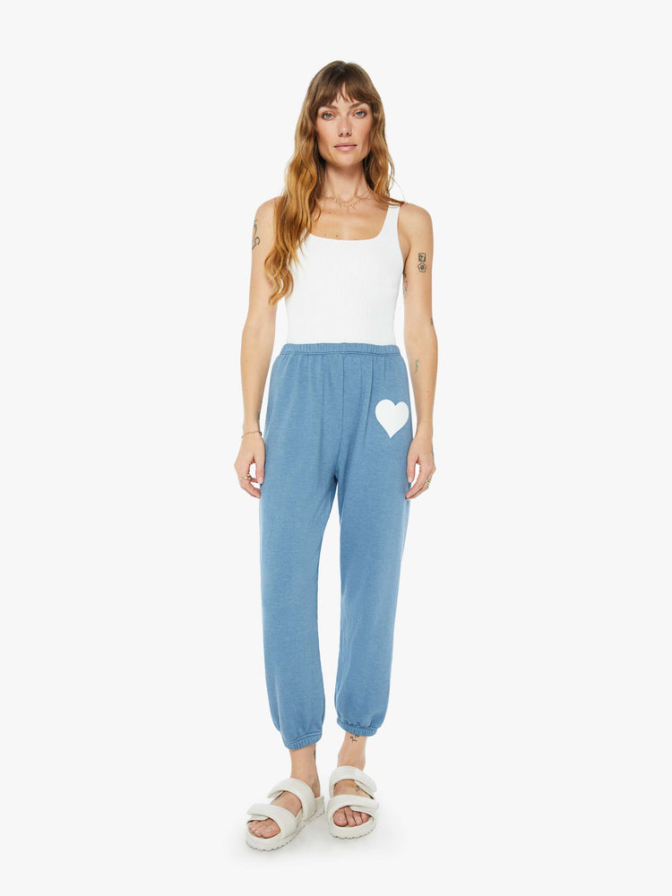 Front view of a womens blue sweatpant featuring an elastic waist and a white heart printed on the hip.