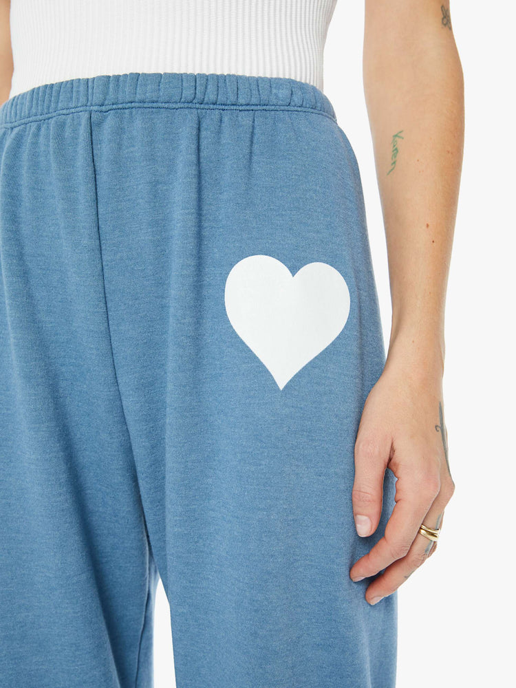 Front close up view of a womens blue sweatpant featuring an elastic waist and a white heart printed on the hip.