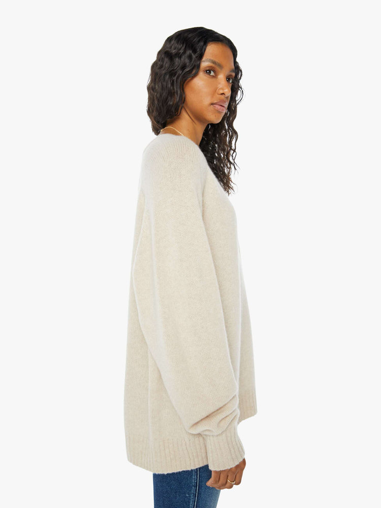 Side view of a  womens beige crew neck knit sweater featuring an oversized fit.