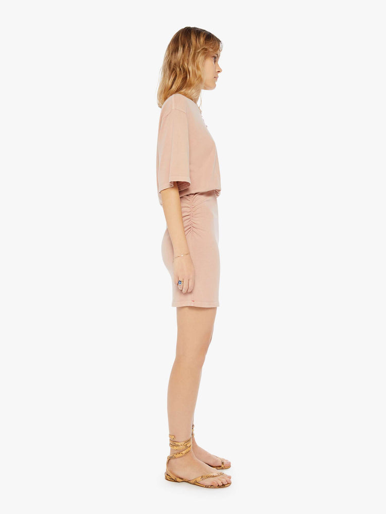 Side view of a woman wearing a pink t-shirt dress with an elastic waistband and ruched skirt