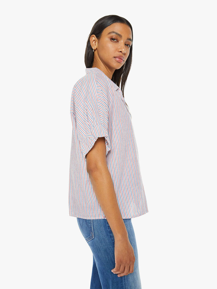 Side view of a woman short-sleeve button-downin red, white and blue stripes with a collared neck, drop shoulders, short sleeves with a rolled hem and a boxy fit.