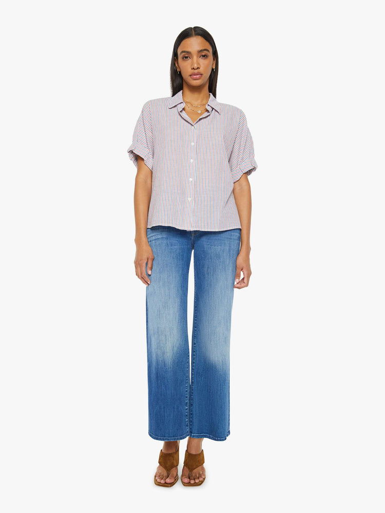 Front full body view of a woman short-sleeve button-downin red, white and blue stripes with a collared neck, drop shoulders, short sleeves with a rolled hem and a boxy fit.