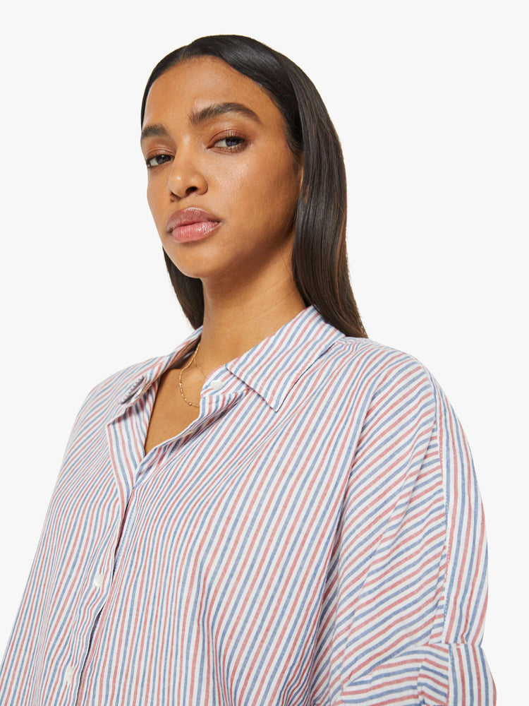 Close up view of a woman short-sleeve button-downin red, white and blue stripes with a collared neck, drop shoulders, short sleeves with a rolled hem and a boxy fit.