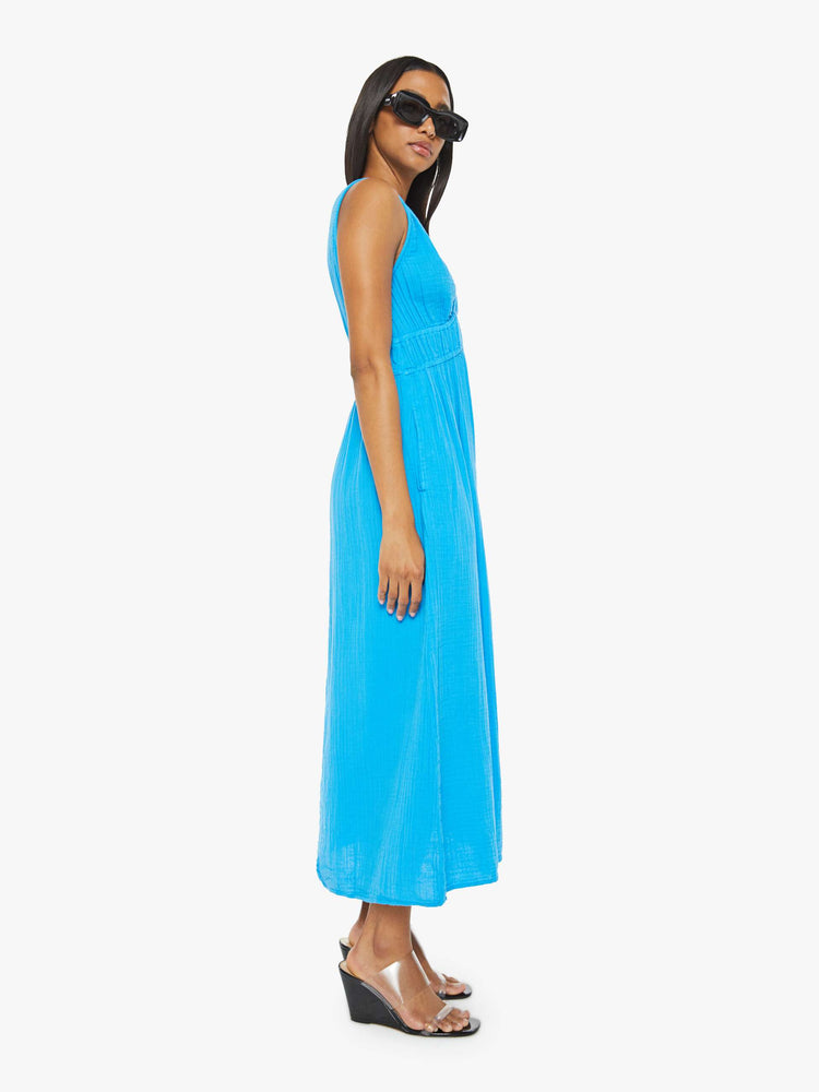 Side view of a woman sleeveless dress in blue, the Arwen dress features a V-neck, gathered, angled seams at the chest and a loose calf-length skirt.