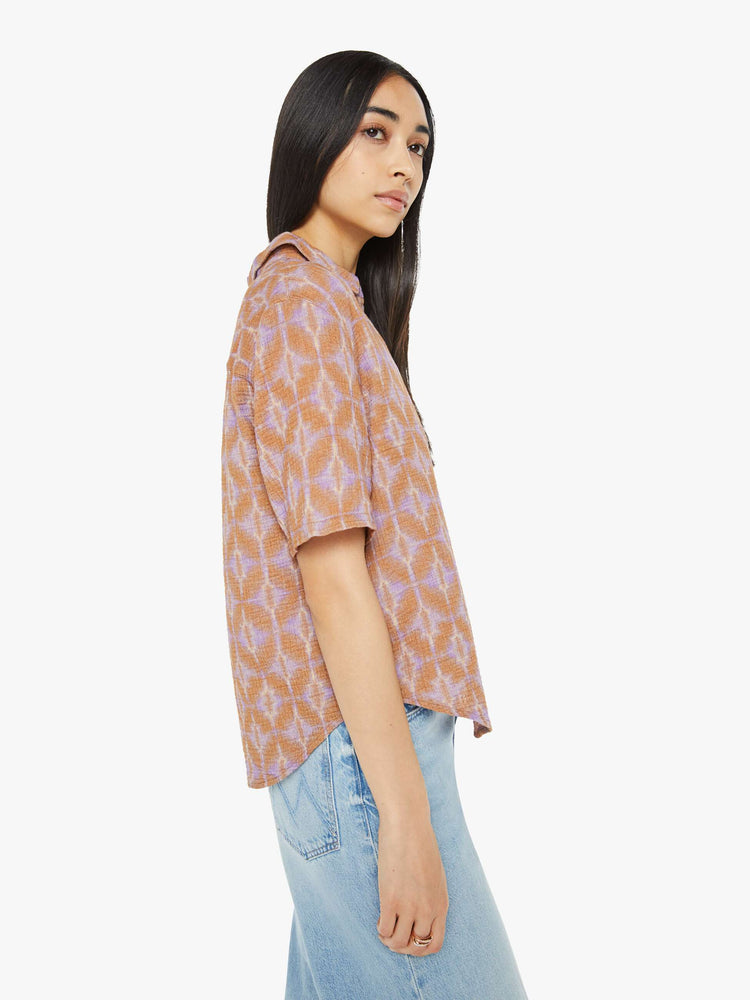 Side view of a woman collared blouse in a terracotta and lavender geometric print, the top is designed with a V-neck, drop shoulders, oversized short sleeves and loose, slightly boxy fit.