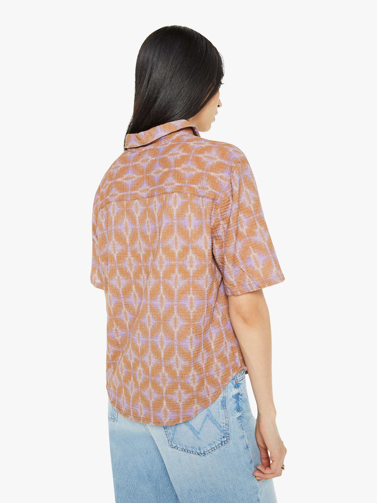 Back view of a woman collared blouse in a terracotta and lavender geometric print, the top is designed with a V-neck, drop shoulders, oversized short sleeves and loose, slightly boxy fit.