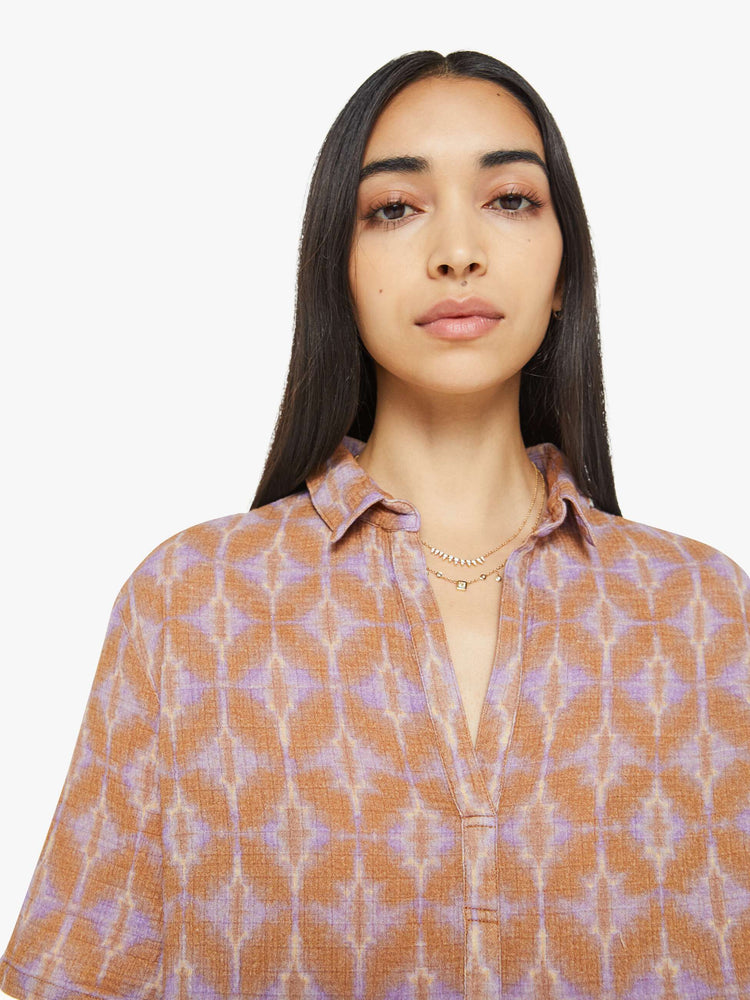 Close up view of a woman collared blouse in a terracotta and lavender geometric print, the top is designed with a V-neck, drop shoulders, oversized short sleeves and loose, slightly boxy fit.