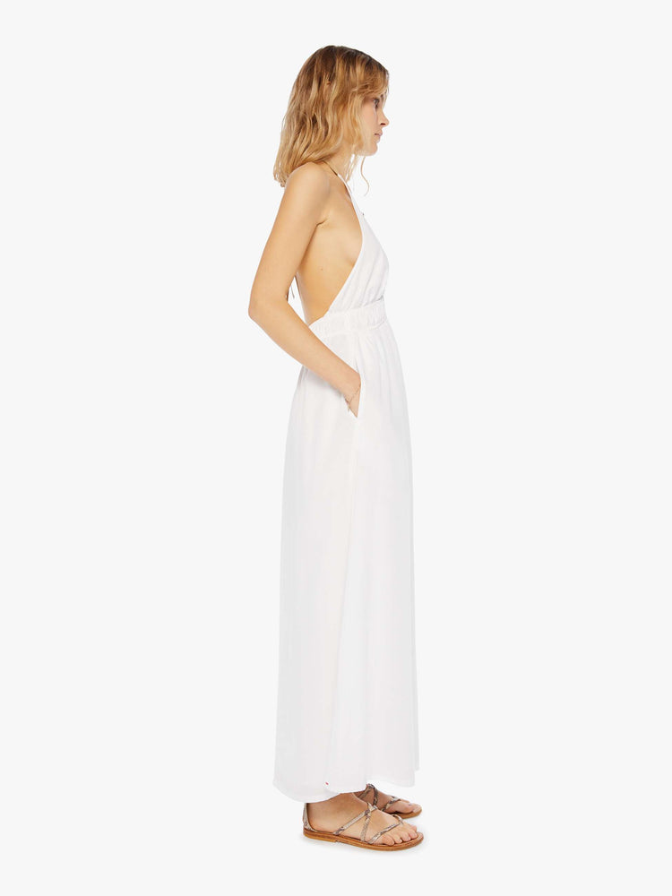 Side view of a womens white ankle length dress featuring a deep v halter neck, side pockets and a full skirt.