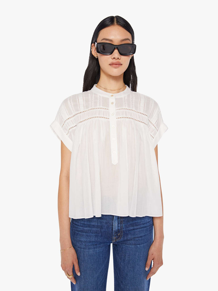 Front view of a white blouse featuring a buttoned mock neck, cuffed short sleeves, eyelet lace details, and a flowy cropped fit.