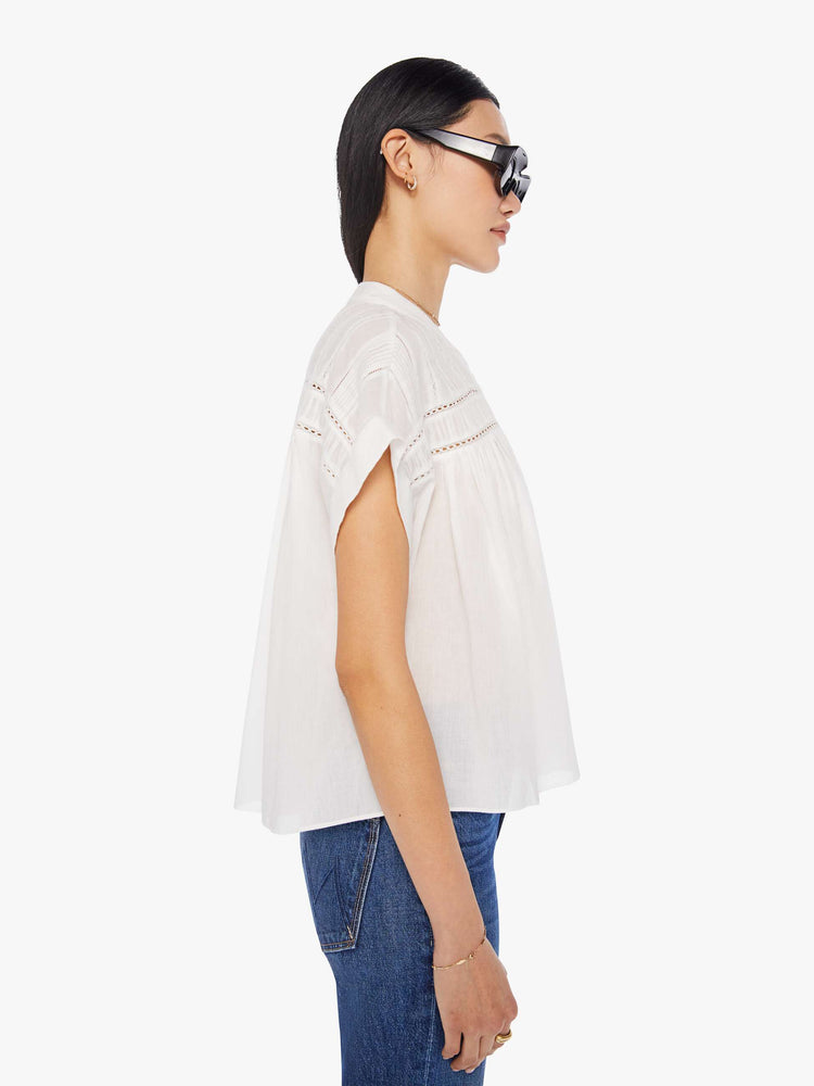 Side view of a white blouse featuring a buttoned mock neck, cuffed short sleeves, eyelet lace details, and a flowy cropped fit.