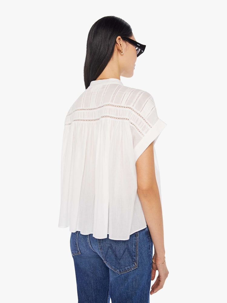 Back view of a white blouse featuring a buttoned mock neck, cuffed short sleeves, eyelet lace details, and a flowy cropped fit.