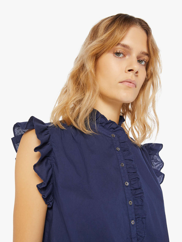 Front close up view of a navy blue blouse featuring a ruffled mock neck and sleeveless ruffles.