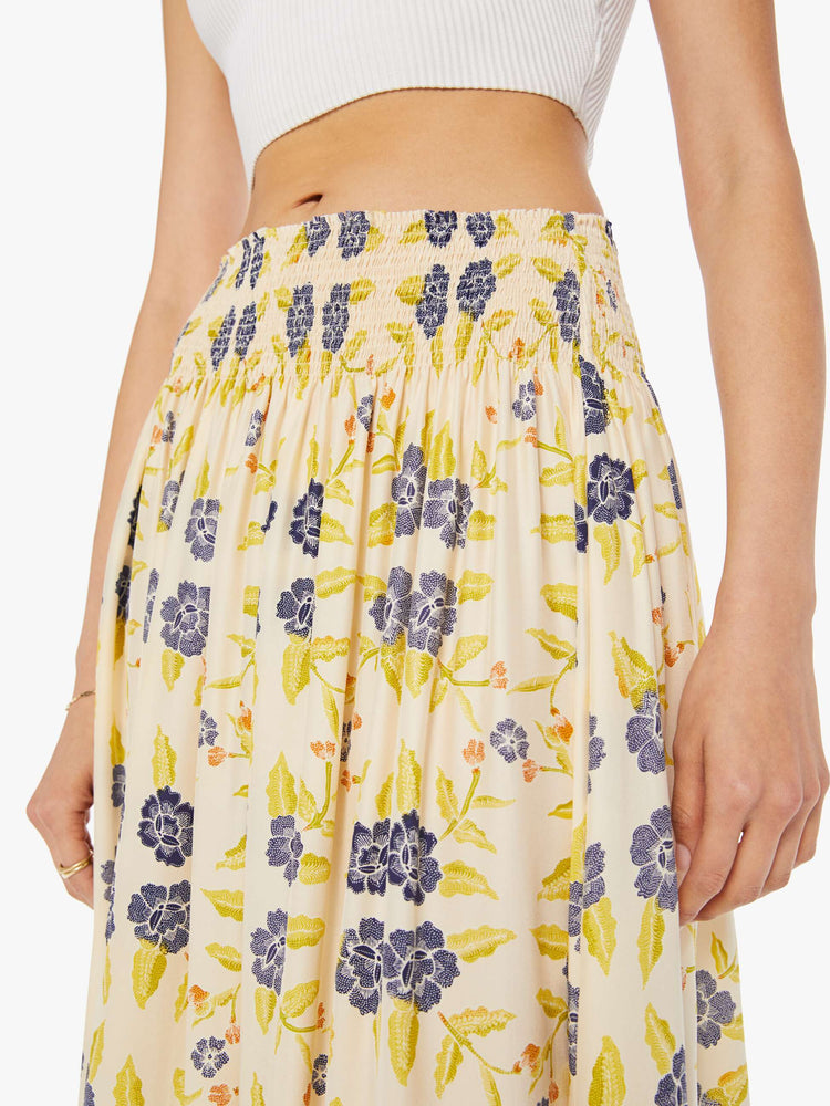 Detail view of a woman wearing a long, off-white skirt with blue floral print and elastic waistband