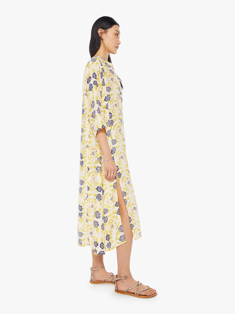 Side view of a woman wearing an off-white maxi dress with blue floral print, 3/4 sleeves, and side slit