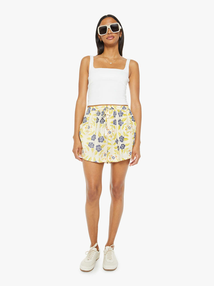 Front view of a woman drawstring shorts in a pale yellow, indigo and white floral print, these lightweight shorts feature an elastic waist with a drawstring, side pockets and scalloped hemline.