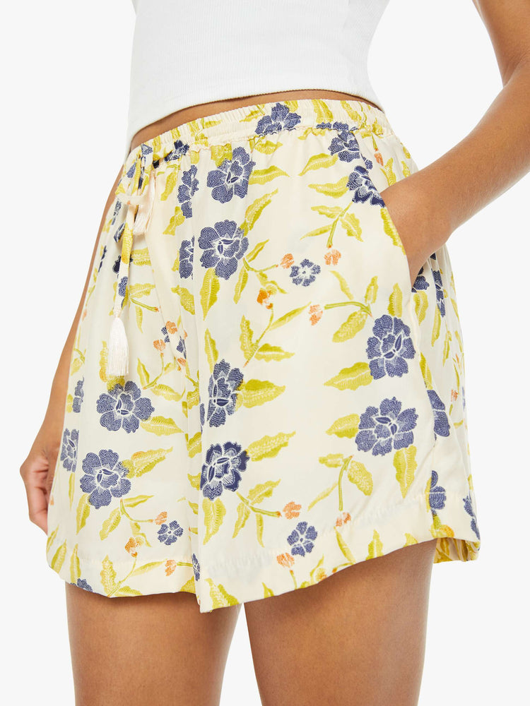 Close up view of a woman drawstring shorts in a pale yellow, indigo and white floral print, these lightweight shorts feature an elastic waist with a drawstring, side pockets and scalloped hemline.