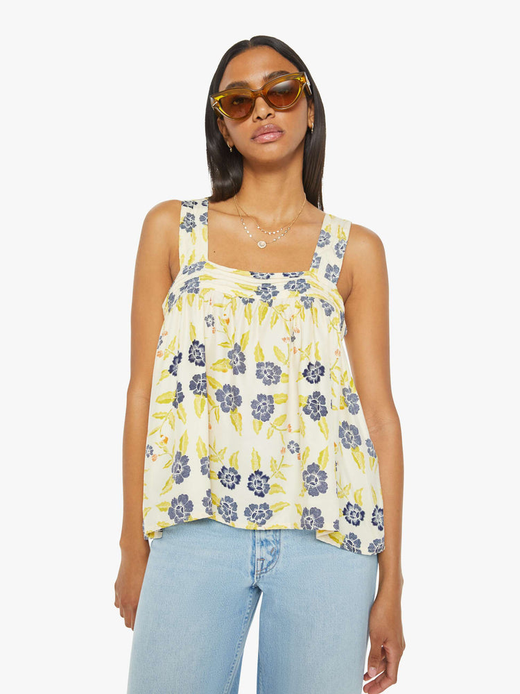 Front view of a woman top in a pale yellow, indigo and white floral print, and features detailed straps and buttons in the back.