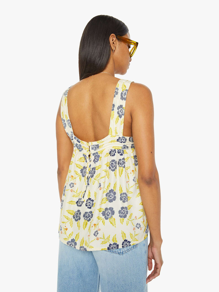 Back view of a woman top in a pale yellow, indigo and white floral print, and features detailed straps and buttons in the back.
