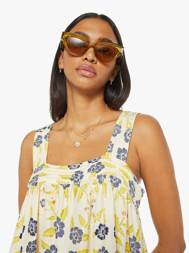 Close up view of a woman top in a pale yellow, indigo and white floral print, and features detailed straps and buttons in the back.