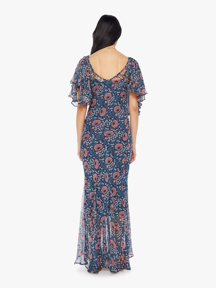 Back view of a woman wearing a full length, blue, chiffon dress with all-over floral print and ruffled sleeves