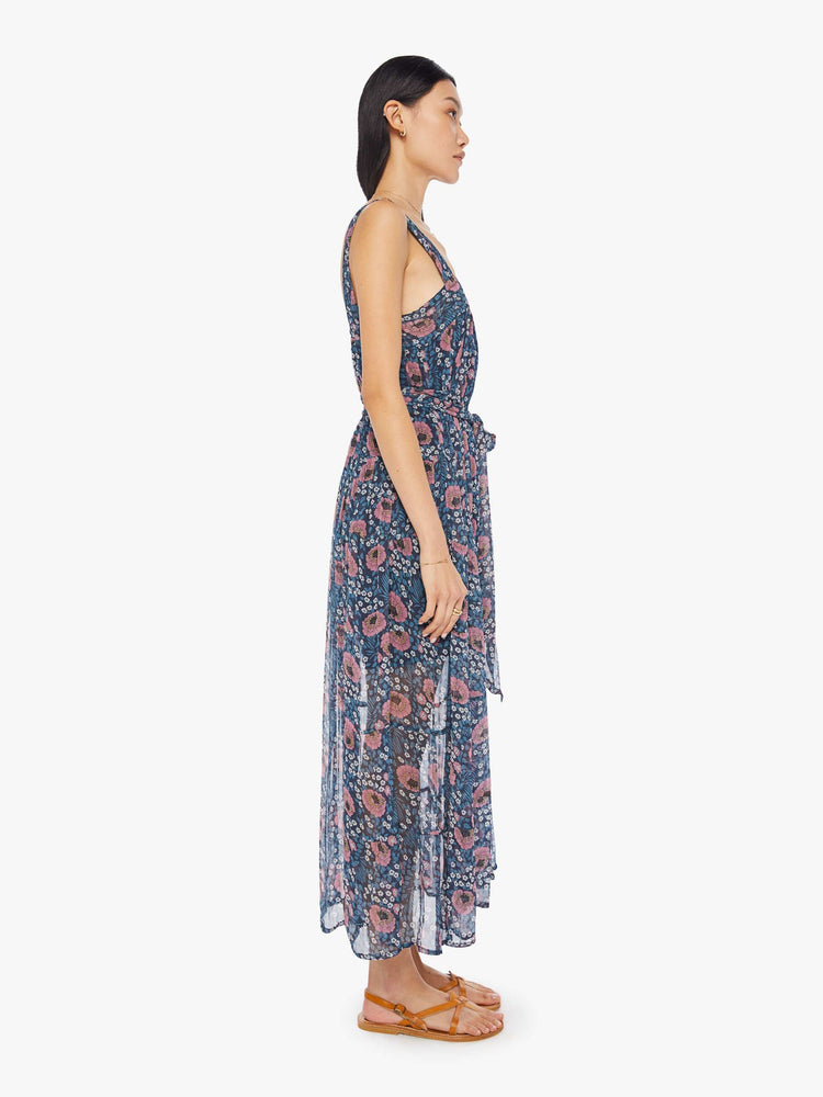 Side view of a woman wearing a blue maxi dress with floral print, square neckline, and sash at the waist