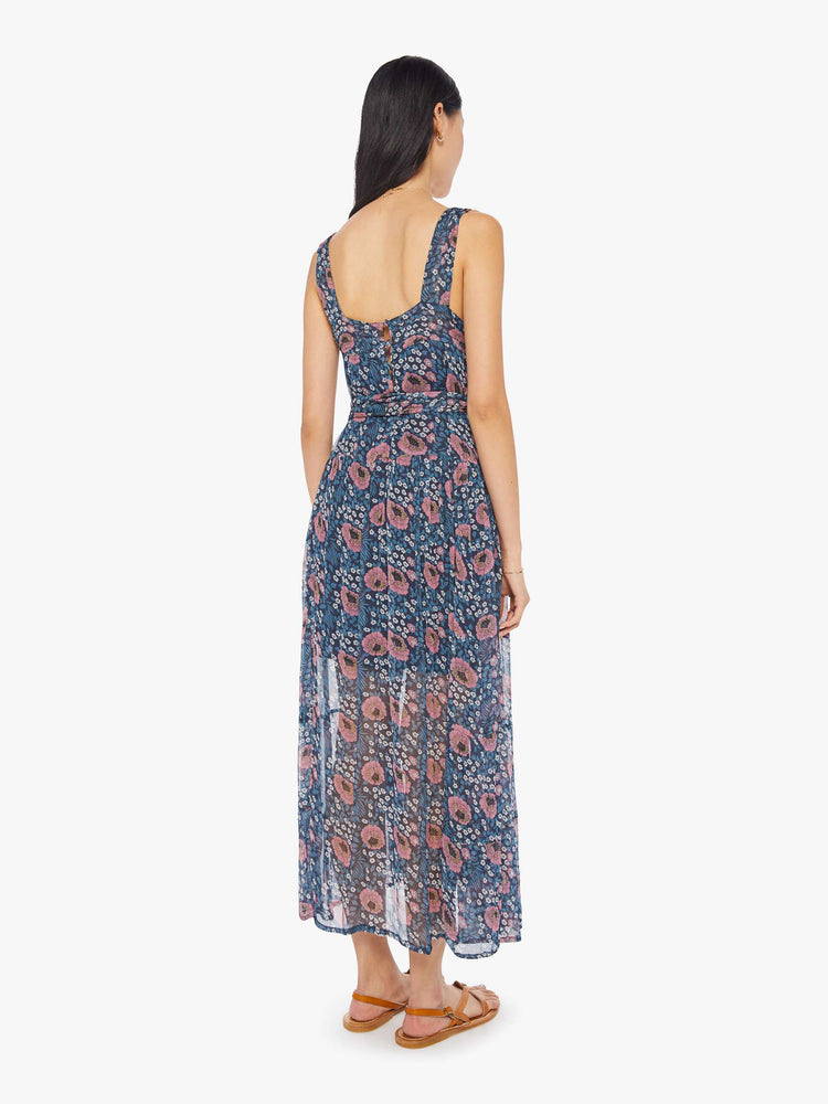 Back view of a woman wearing a blue maxi dress with floral print, square neckline, and sash at the waist
