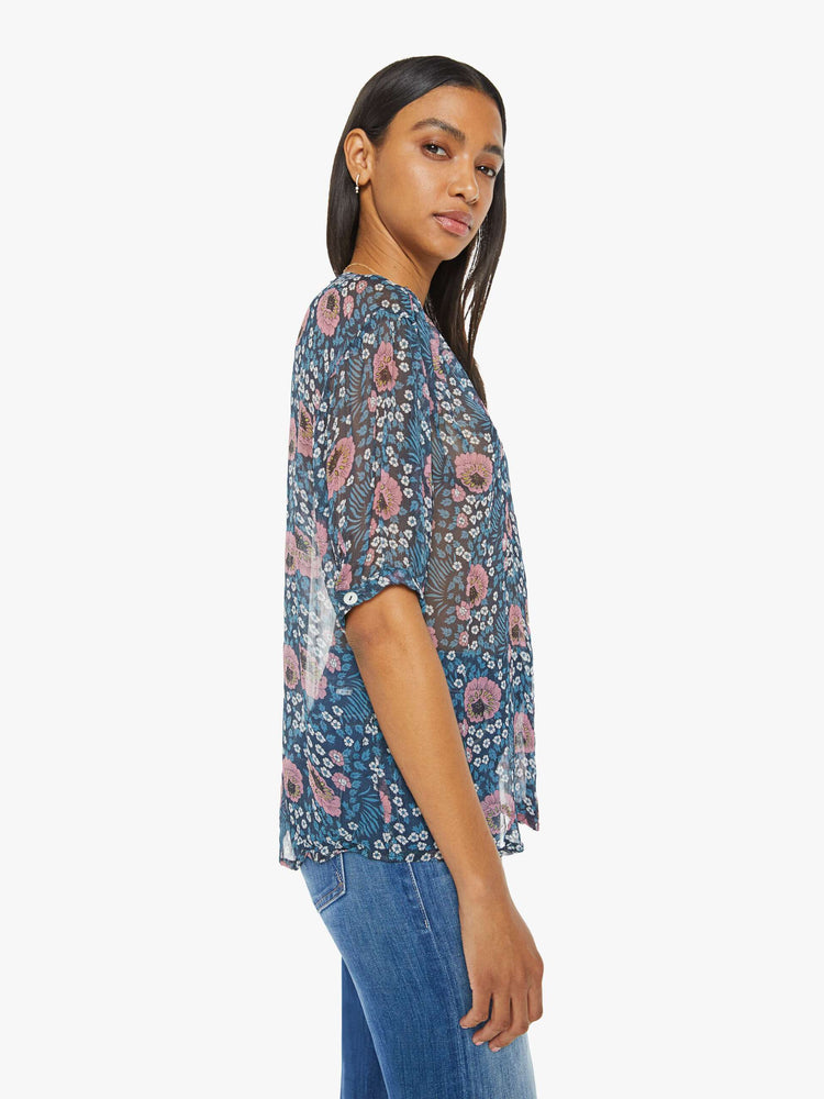Side view of a woman top in dark teal with a pink and white vintage-inspired floral print, and features a deep V-neck, drop shoulders, elbow-length sleeves, a curved hem and a loose, flowy fit.
