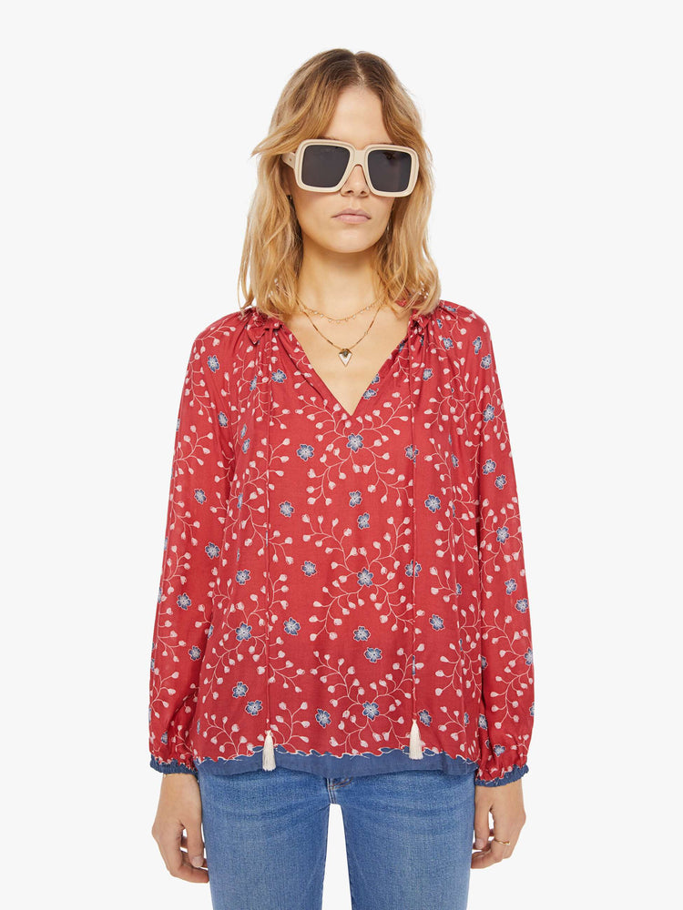 Front view of a woman wearing a red blouse with blue floral print, long sleeves, and tassel closure at the neckline