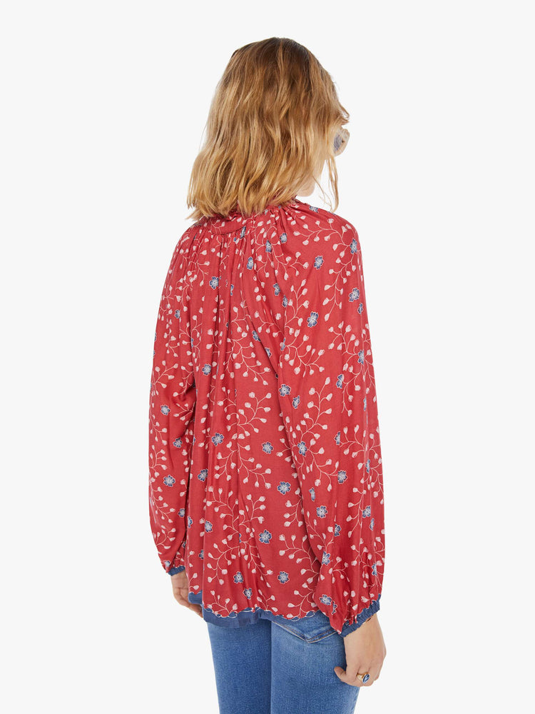 Back view of a woman wearing a red blouse with blue floral print, long sleeves, and tassel closure at the neckline