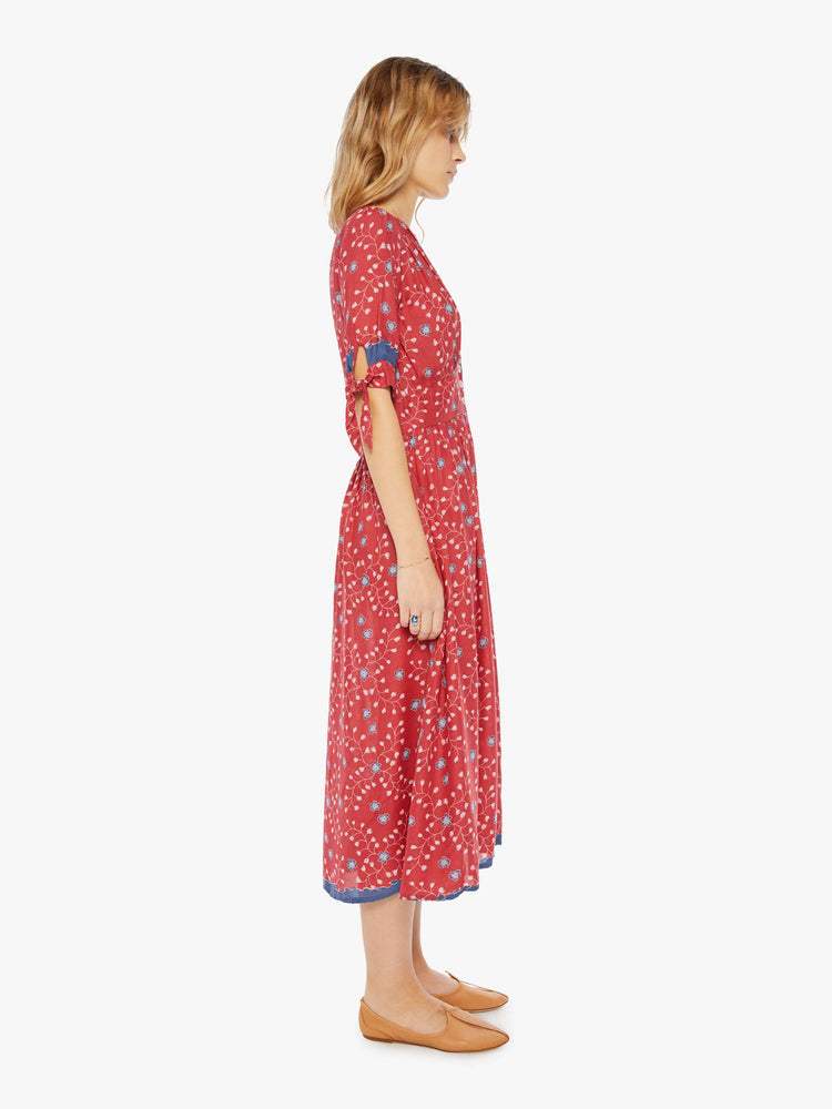 Side view of a woman wearing a red button up dress with blue floral print and elbow length sleeves