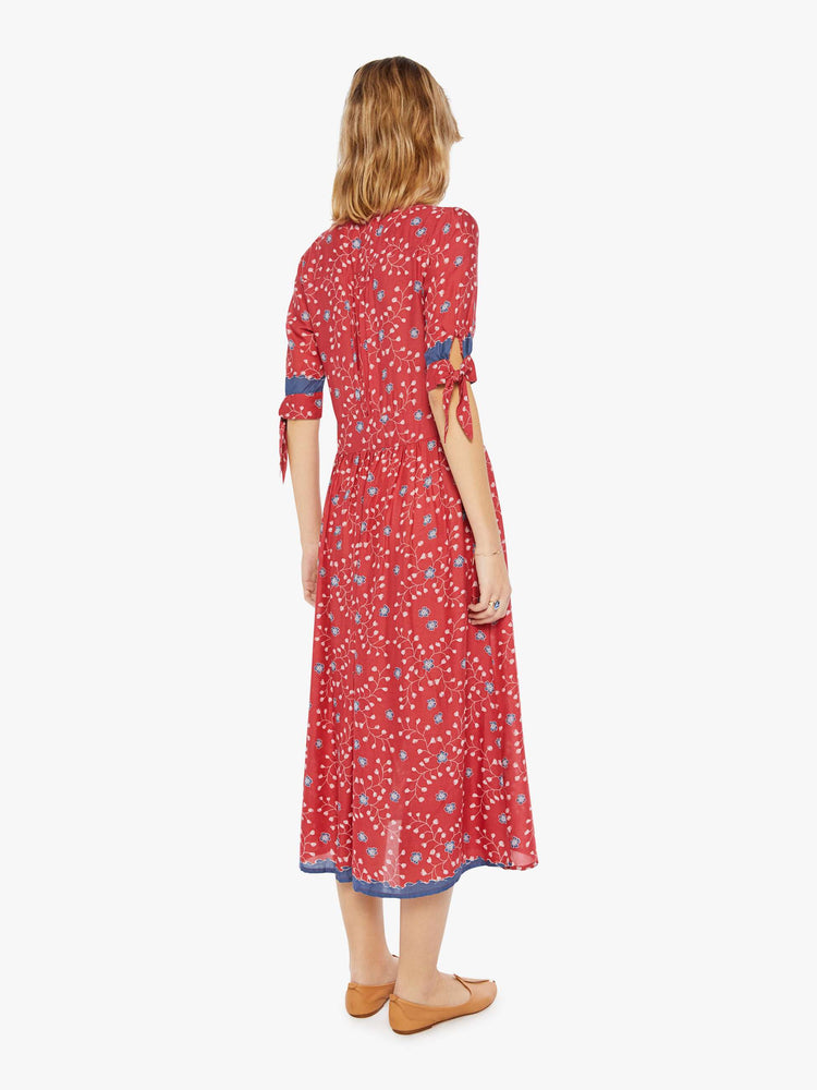 Back view of a woman wearing a red button up dress with blue floral print and elbow length sleeves