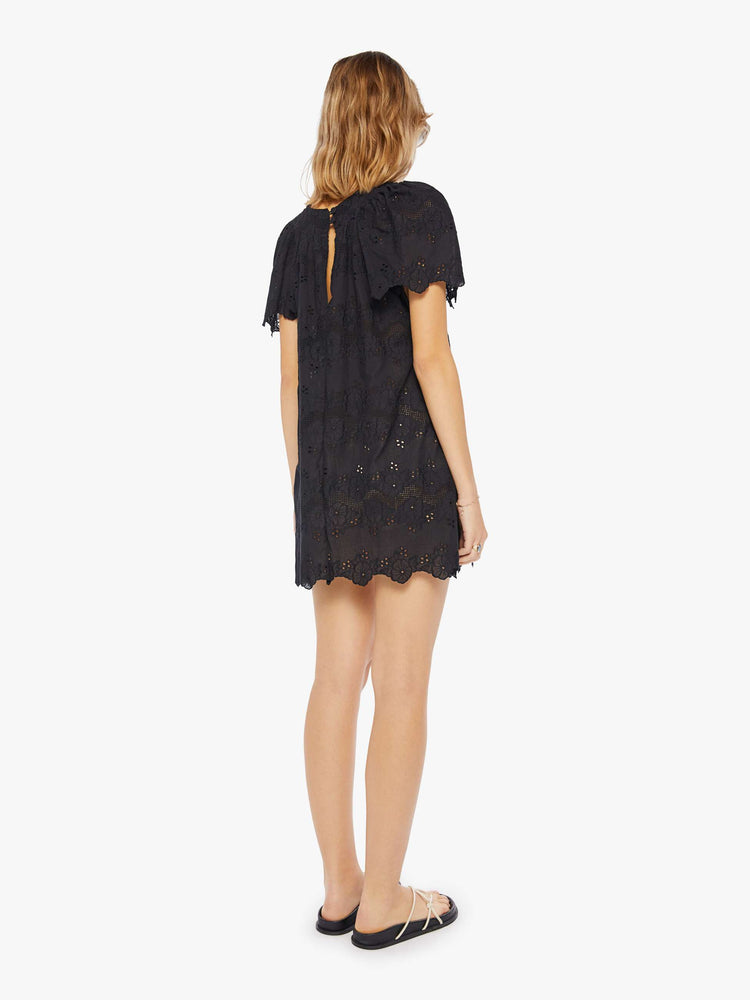 Back view of a woman wearing a short black dress with scoop neckline, short sleeves, and eyelet detail